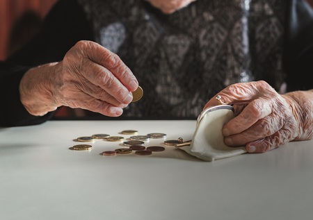 Elderly 95 years old woman sitting miserably at the table at home and counting remaining coins from the pension in her wallet after paying the bills.